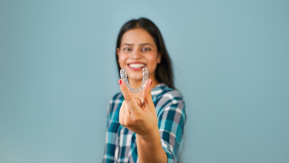 Une femme montre ses gouttières Invisalign au premier plan